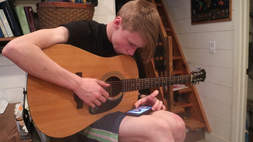 teen playing guitar while looking at online guitar lesson