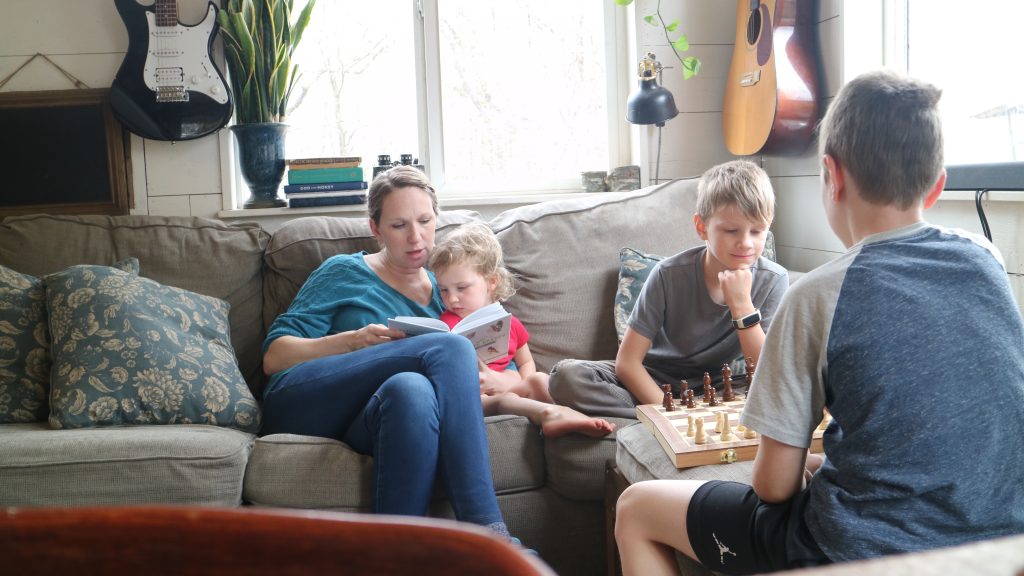 Mom reading to child while boys play chess